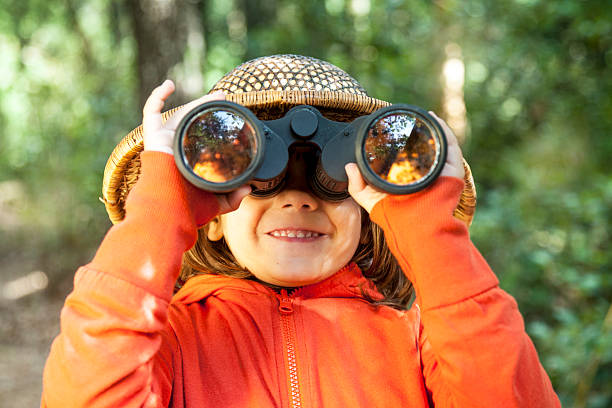 Young girl in orange coat looking through binoculars